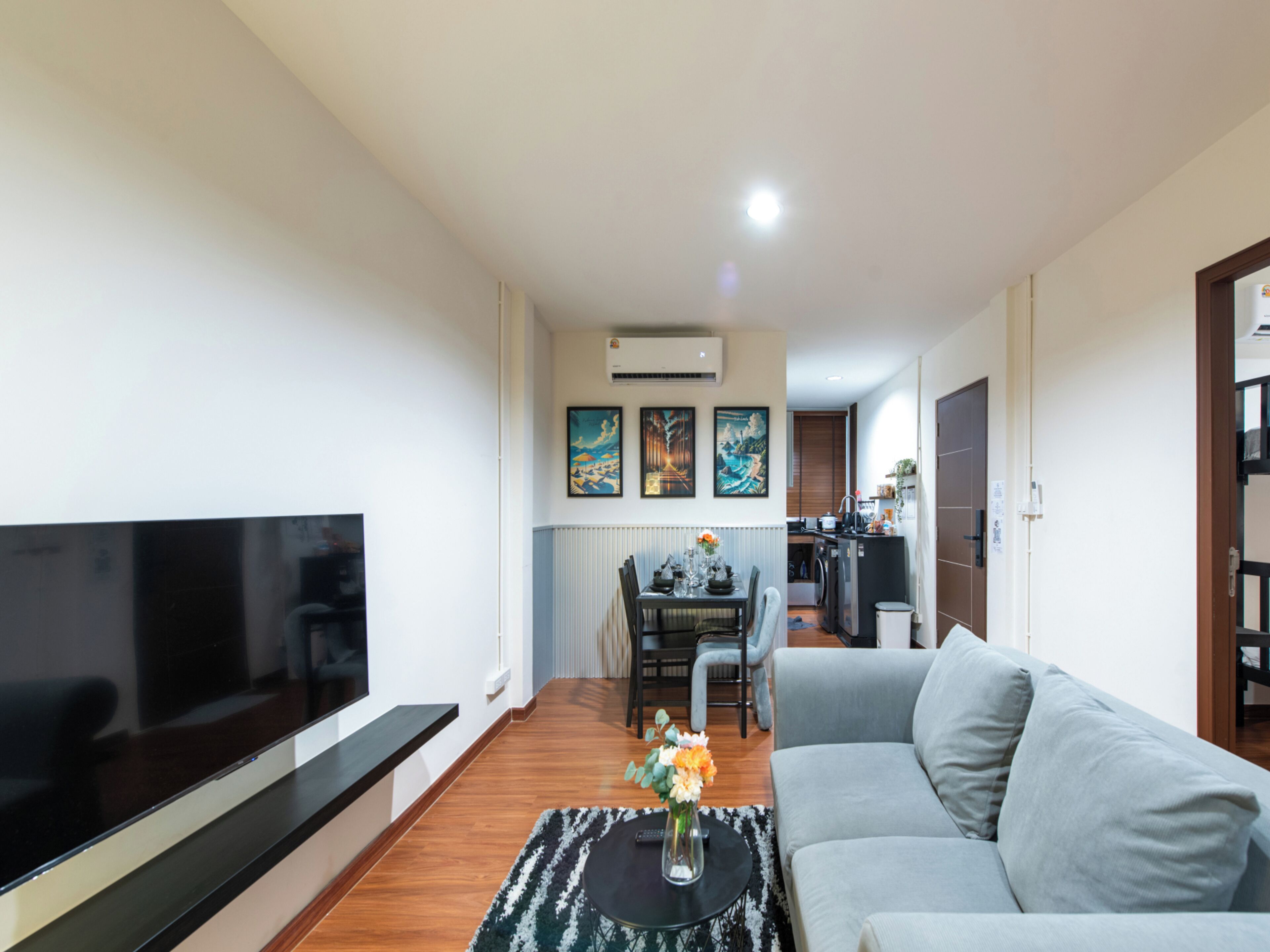 A modern living room with a flat-screen TV, a gray sofa, and a dining area with a table and chairs.