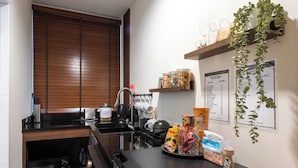 Een kleine keuken met een magnetron, broodrooster, waterkoker en een spoelbak. Er staan planken met potten en een menukaart aan de muur.