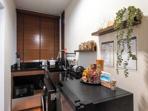 A compact kitchen with a microwave, toaster, kettle, and a sink. There are shelves with jars and a menu on the wall. - The City Yaowarat (Bangkok)
