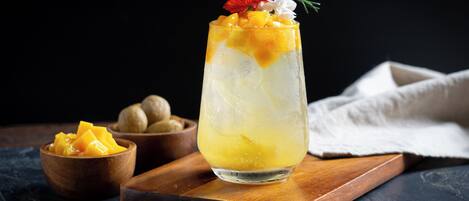 Un vaso alto con una bebida en capas, decorado con frutas y flores, sobre una tabla de madera con fondo oscuro.