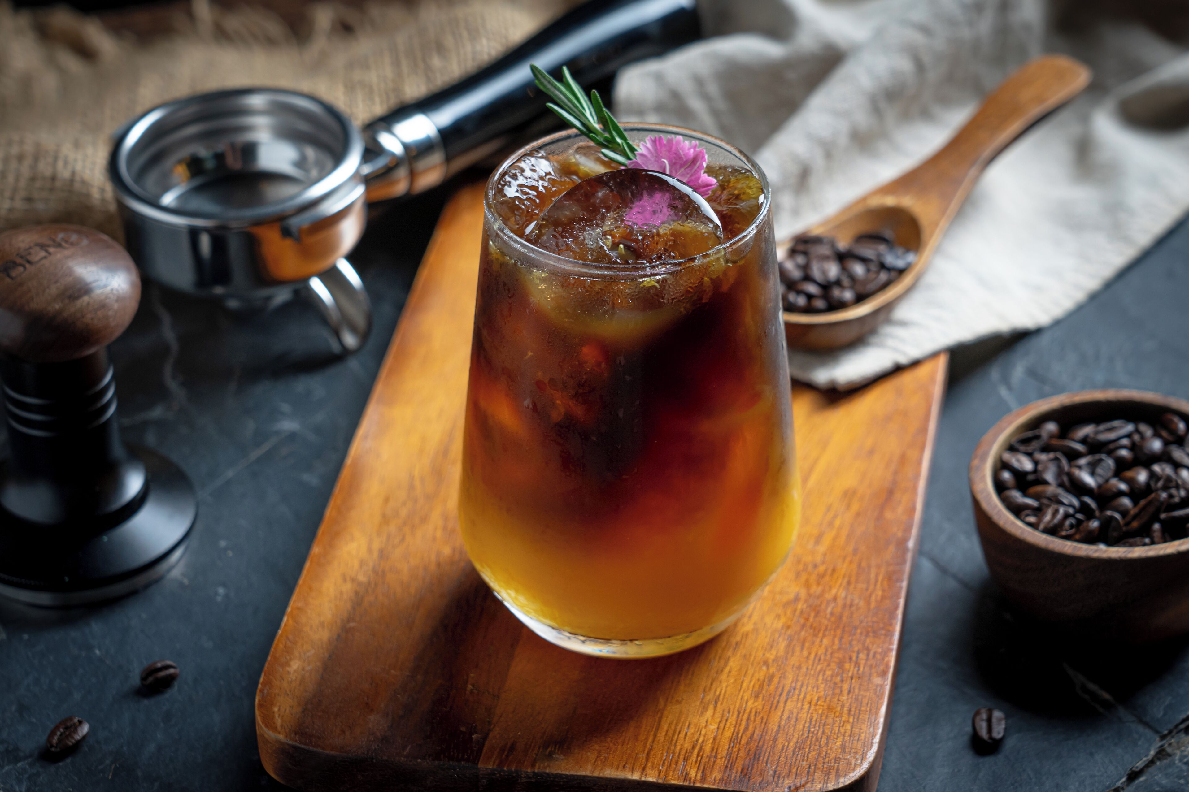 A glass of iced tea with a flower garnish on a wooden tray.