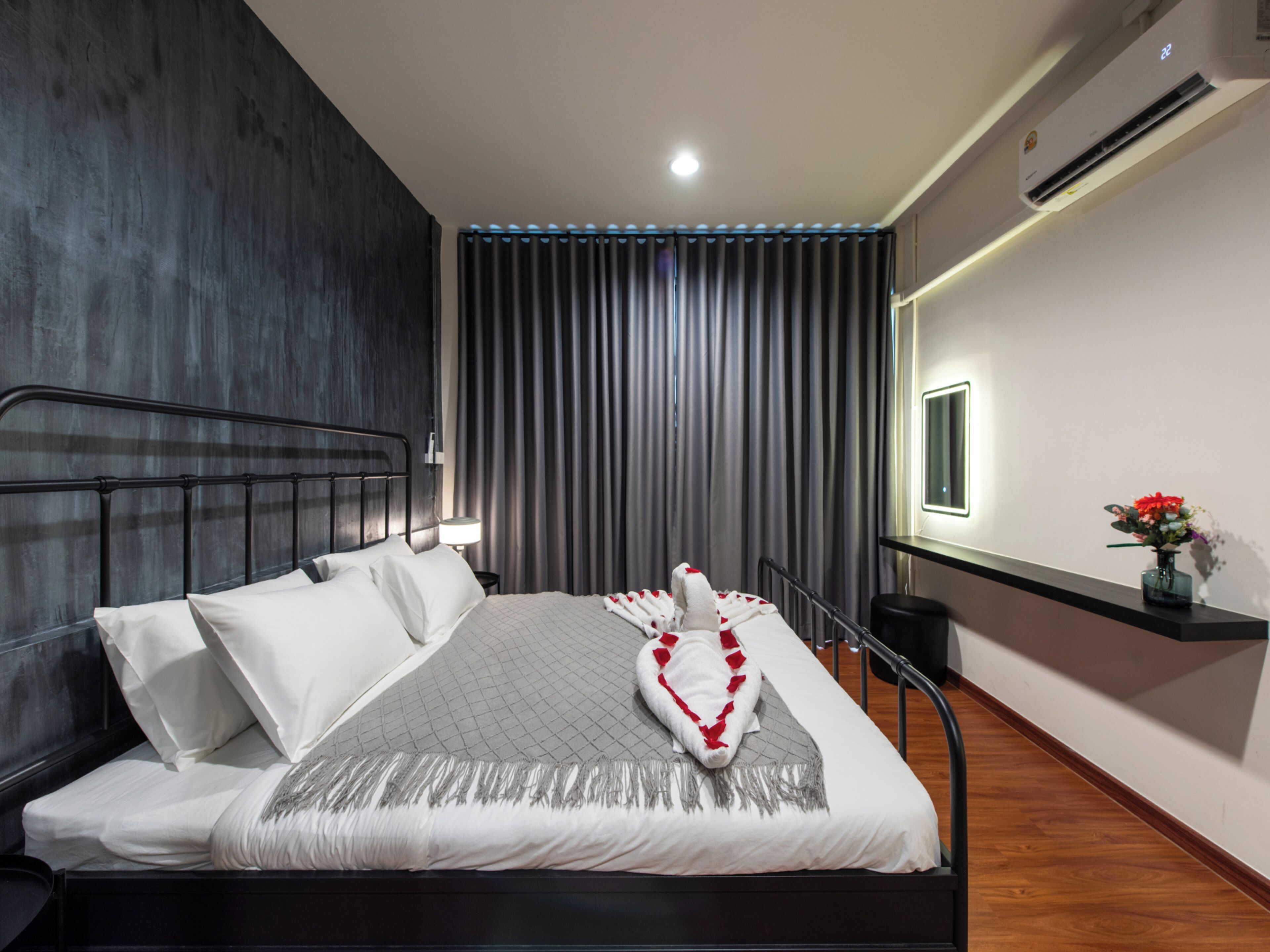 A modern hotel room with a bed, a nightstand, a lamp, a window, and an air conditioning unit.