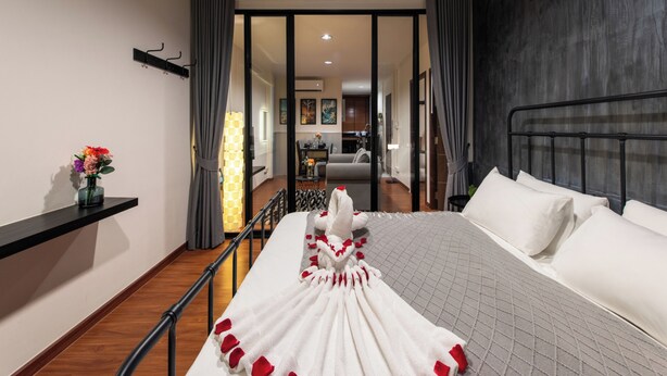 Hotelkamer met een bed, een nachtkastje met een bloevas, uitzicht op de zithoek door een glazen deur, en een modern design met een donkere accentmuur.