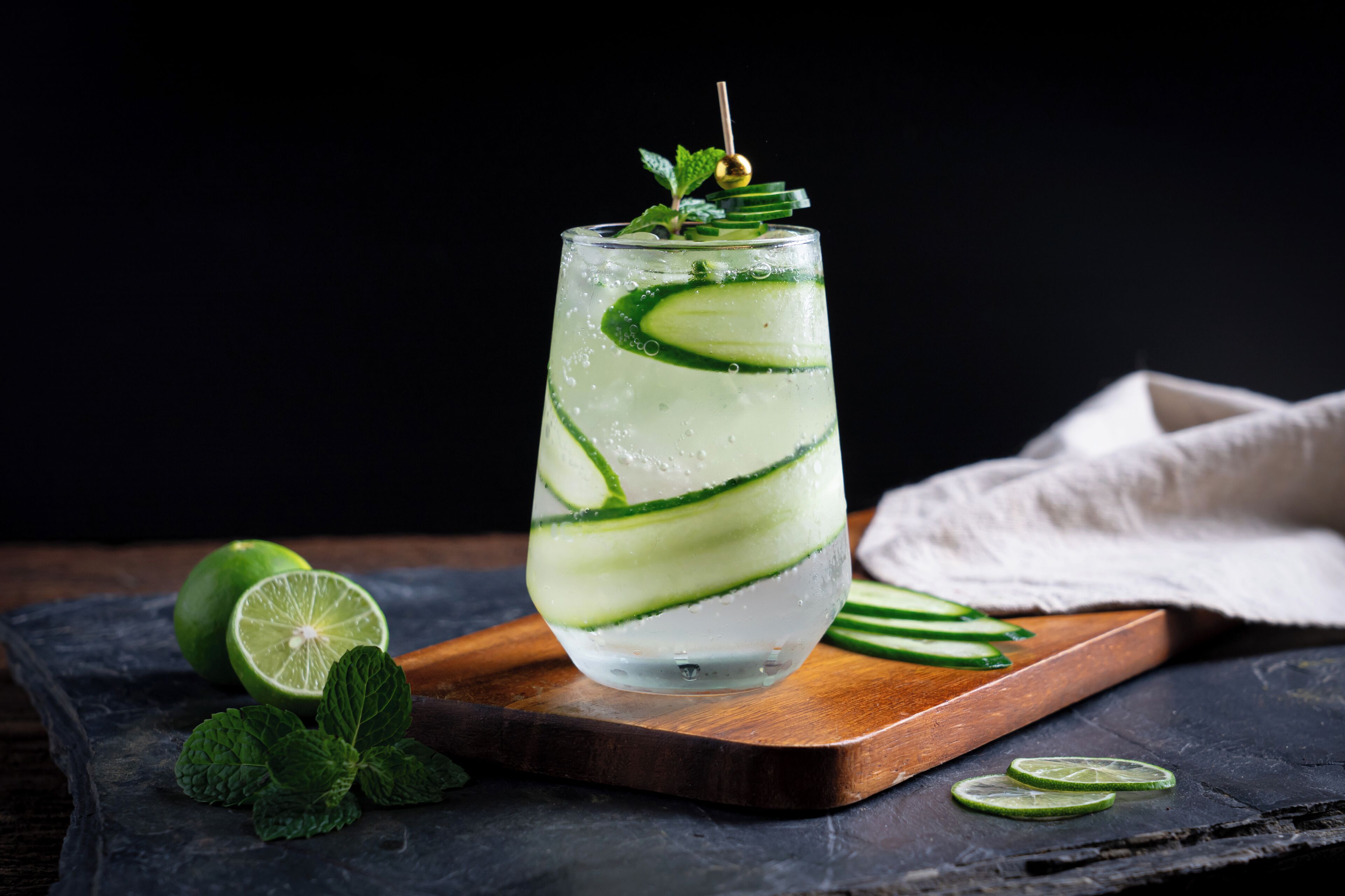 A glass of a beverage with lime slices and mint garnish on a wooden board.