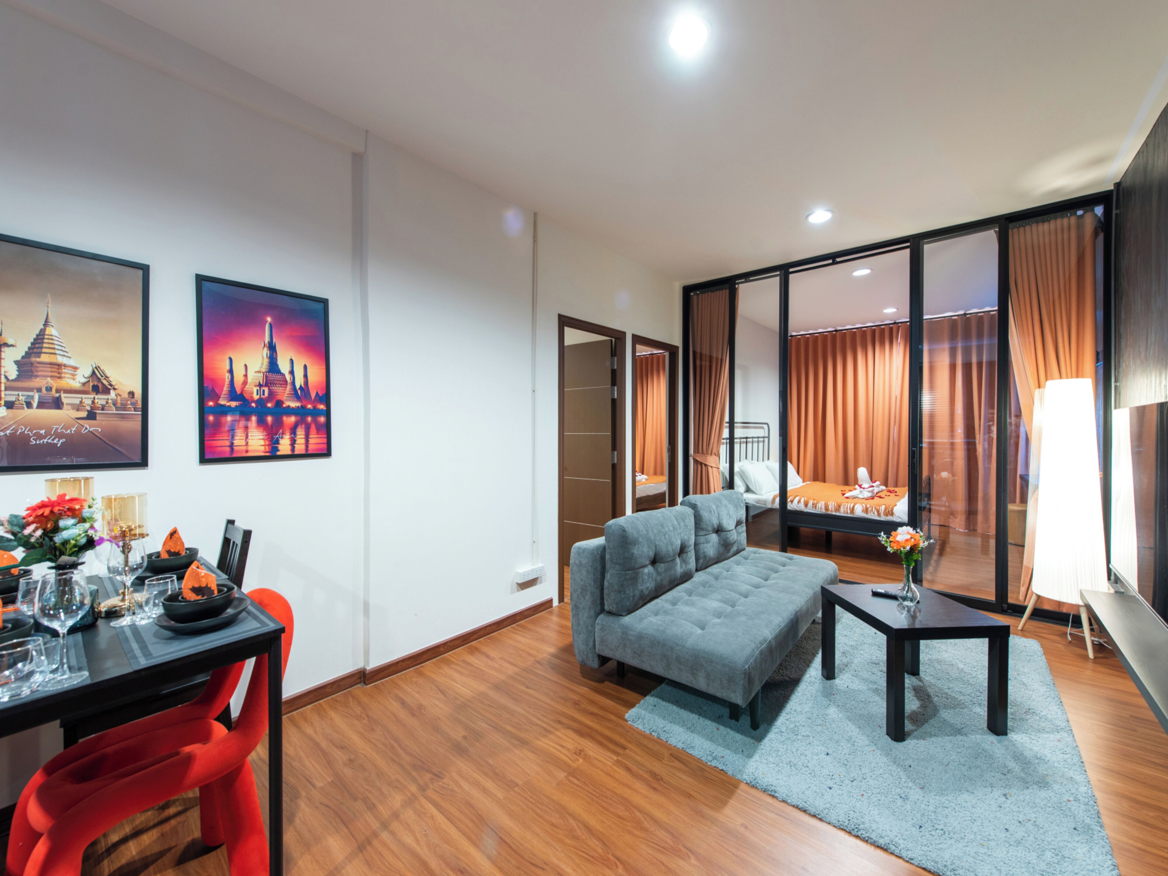 A modern living room with a grey sofa, a dining table with chairs, and a bed with curtains.