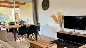 A modern living room with a sofa, a wooden coffee table, a TV, and a dining area with chairs and a table. - The Montchamp villa (Chambonas)