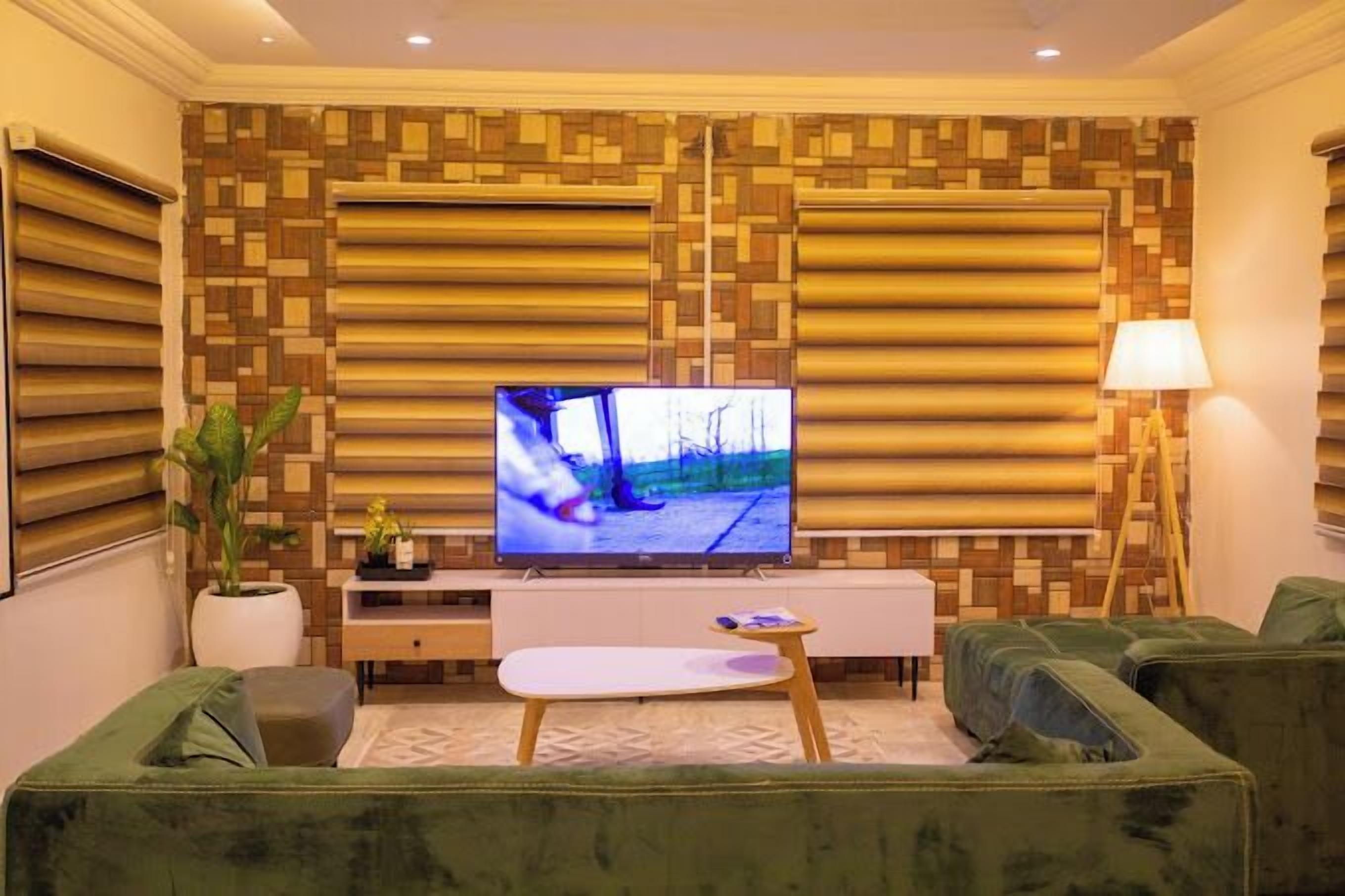 Ein modernes Wohnzimmer mit Flachbildfernseher, grünen Sofas, einem weißen Konsolentisch und einer Wand mit Musterung.