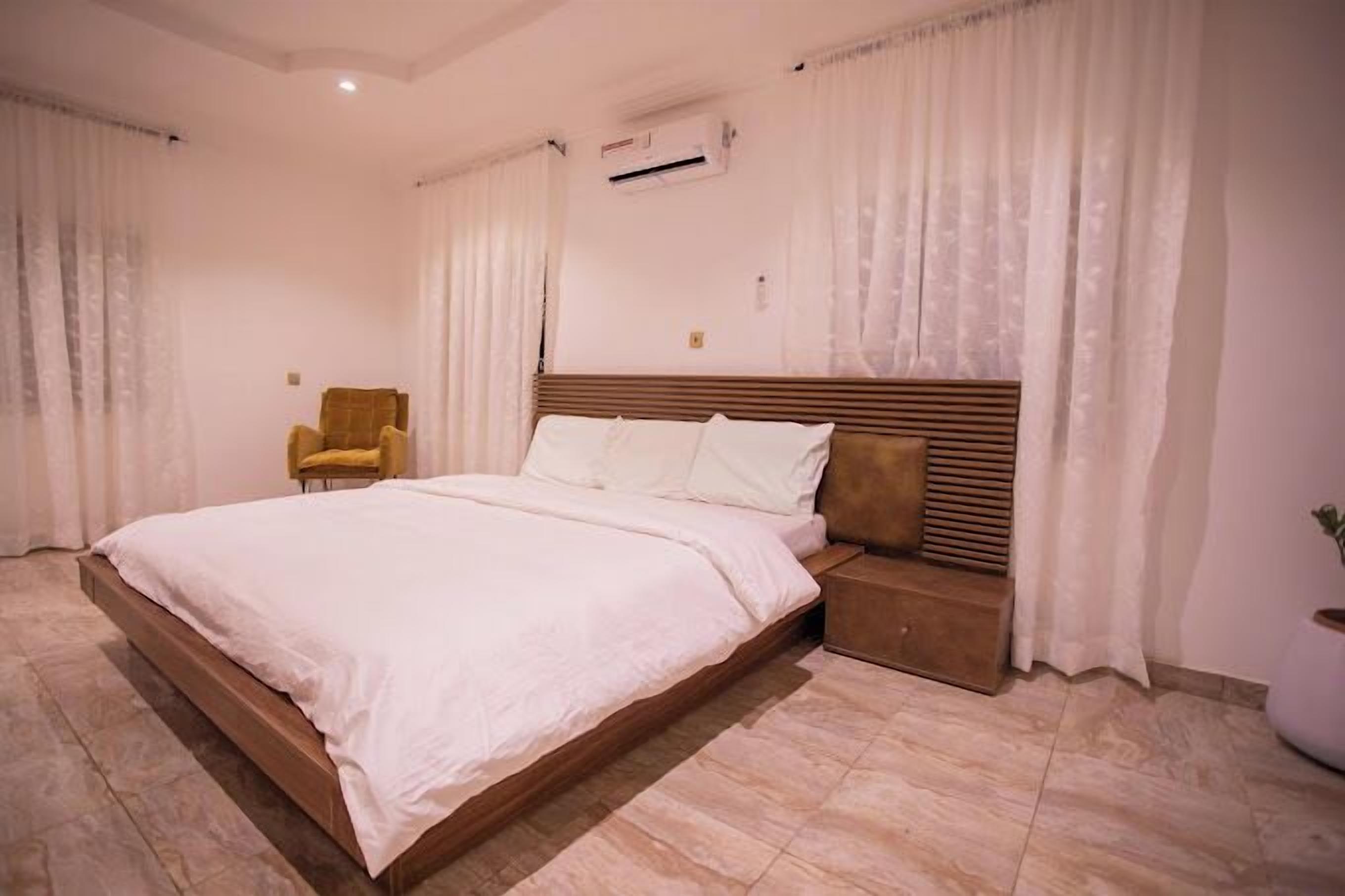 A bedroom with a large bed, a bedside table, a chair, and a potted plant.