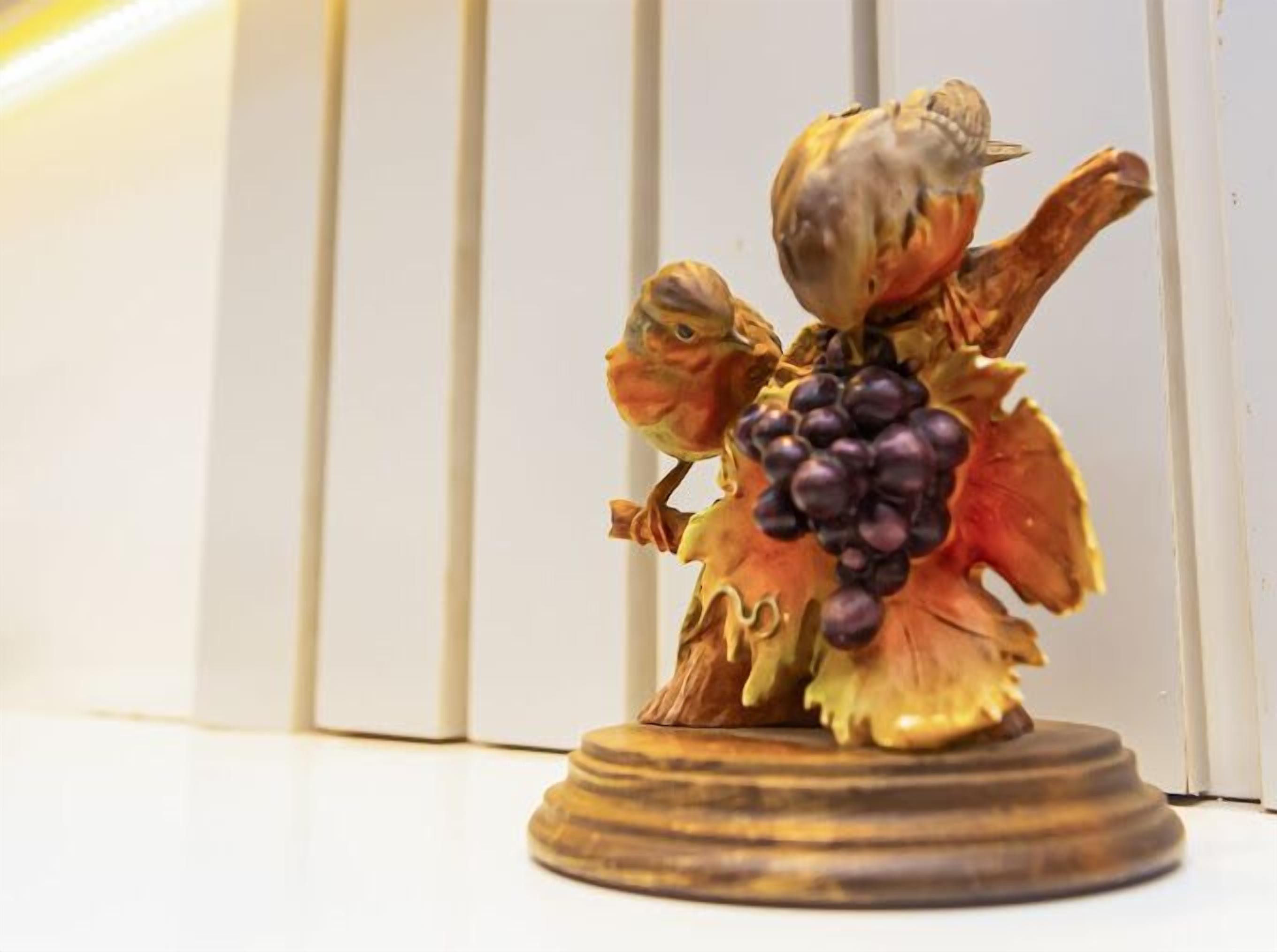 A wooden statue of a person holding a bunch of grapes, placed on a round wooden base.