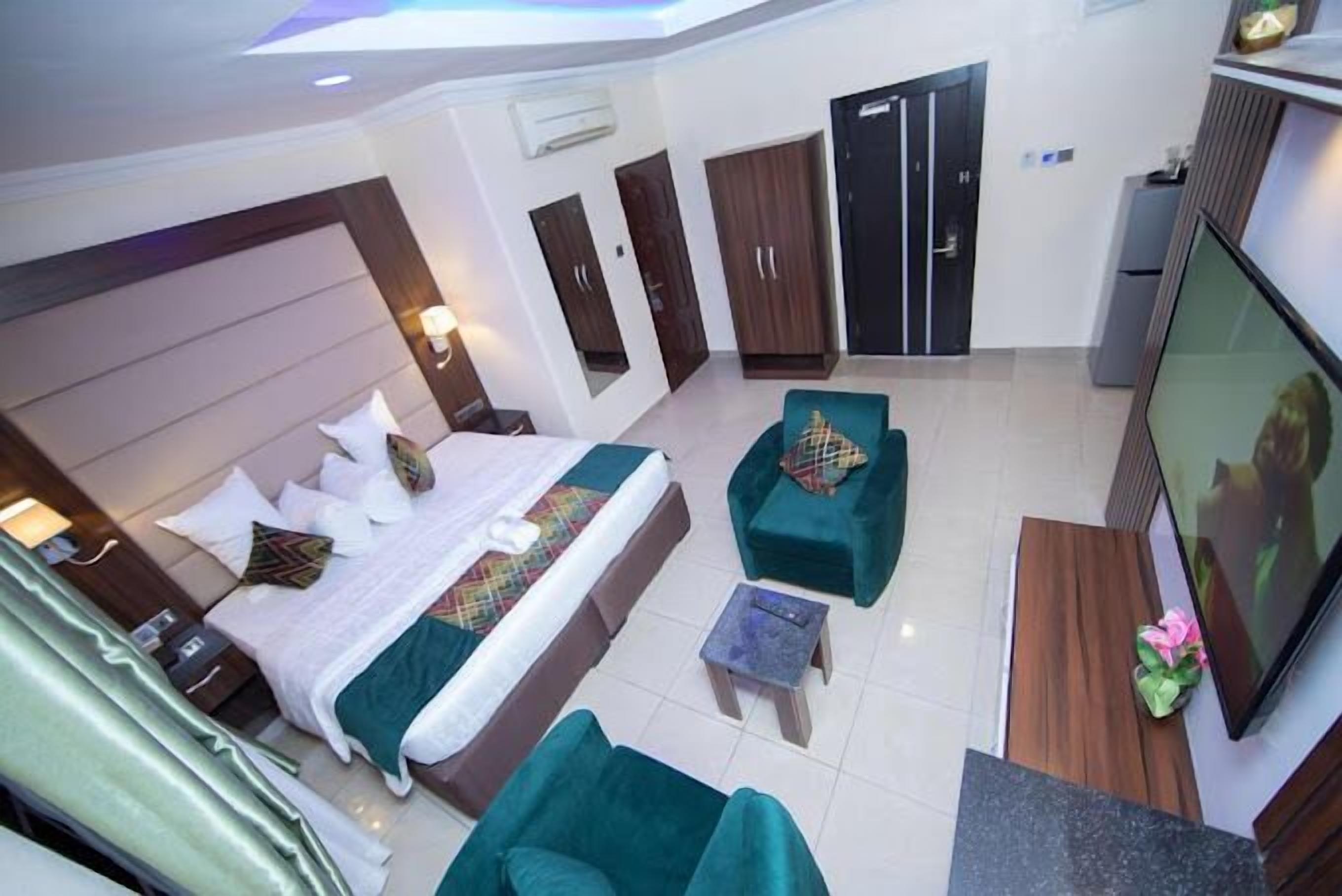 Habitación de hotel con una cama grande, dos sillones verdes, una mesita, un televisor y un armario.