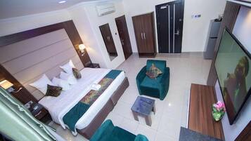 Habitación de hotel con una cama grande, dos sillones verdes, una mesita, un televisor y un armario.