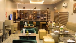 A restaurant with green upholstered chairs, tables with white plates, and a bar area with shelves of bottles. - Class Suites Hotel and Apartment (Abuja)