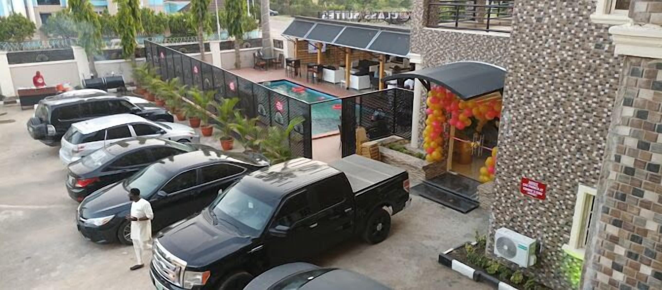 A parking area with several cars, a pool area with lounge chairs, and a building with a stone facade.