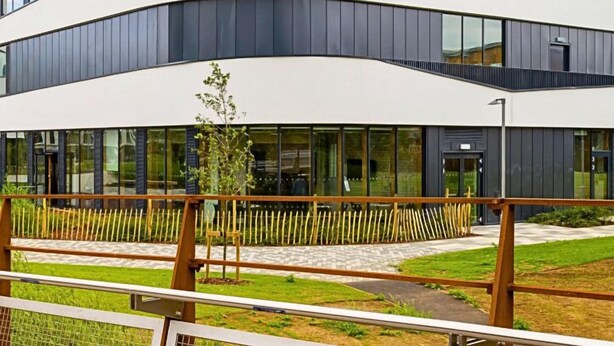 A modern building with the 'University of Northampton' sign, featuring a curved facade, large windows, and a grassy area in front.