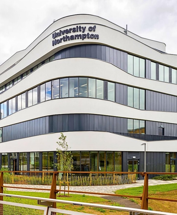 Un edificio moderno con el letrero 'University of Northampton', que presenta una fachada curva, ventanas amplias y un área verde frente a él.