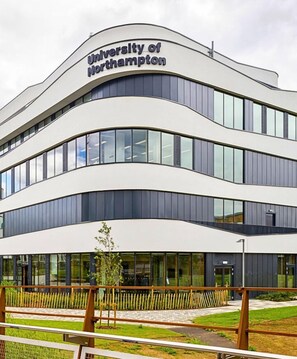 A modern building with the 'University of Northampton' sign, featuring a curved facade, large windows, and a grassy area in front. - Grange House • Sleeps 6 • Driveway Parking • Sky TV • Fast WiFi • Self-Check-In • Yoko Property (West Northamptonshire)