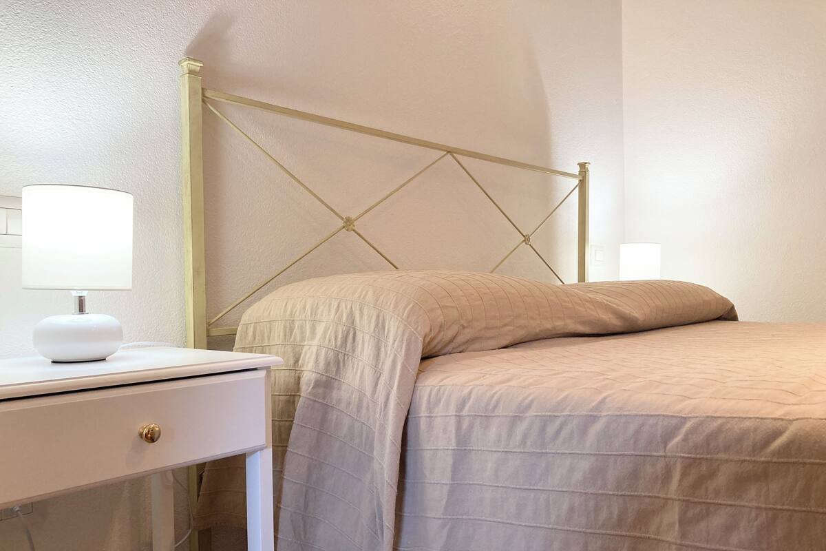 Een slaapkamer met een bed, nachtkastje, lamp en een wandlamp.