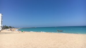A beach with a clear sky, a sandy shore, and a building with balconies. - Comfortable house 100m from the wild beaches of Peniscola Sud. Pets allowed (VC)