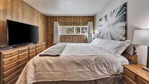 Un dormitorio con una cama grande, paredes de paneles de madera, un televisor de pantalla plana, una ventana con cortinas y un cuadro en la pared.