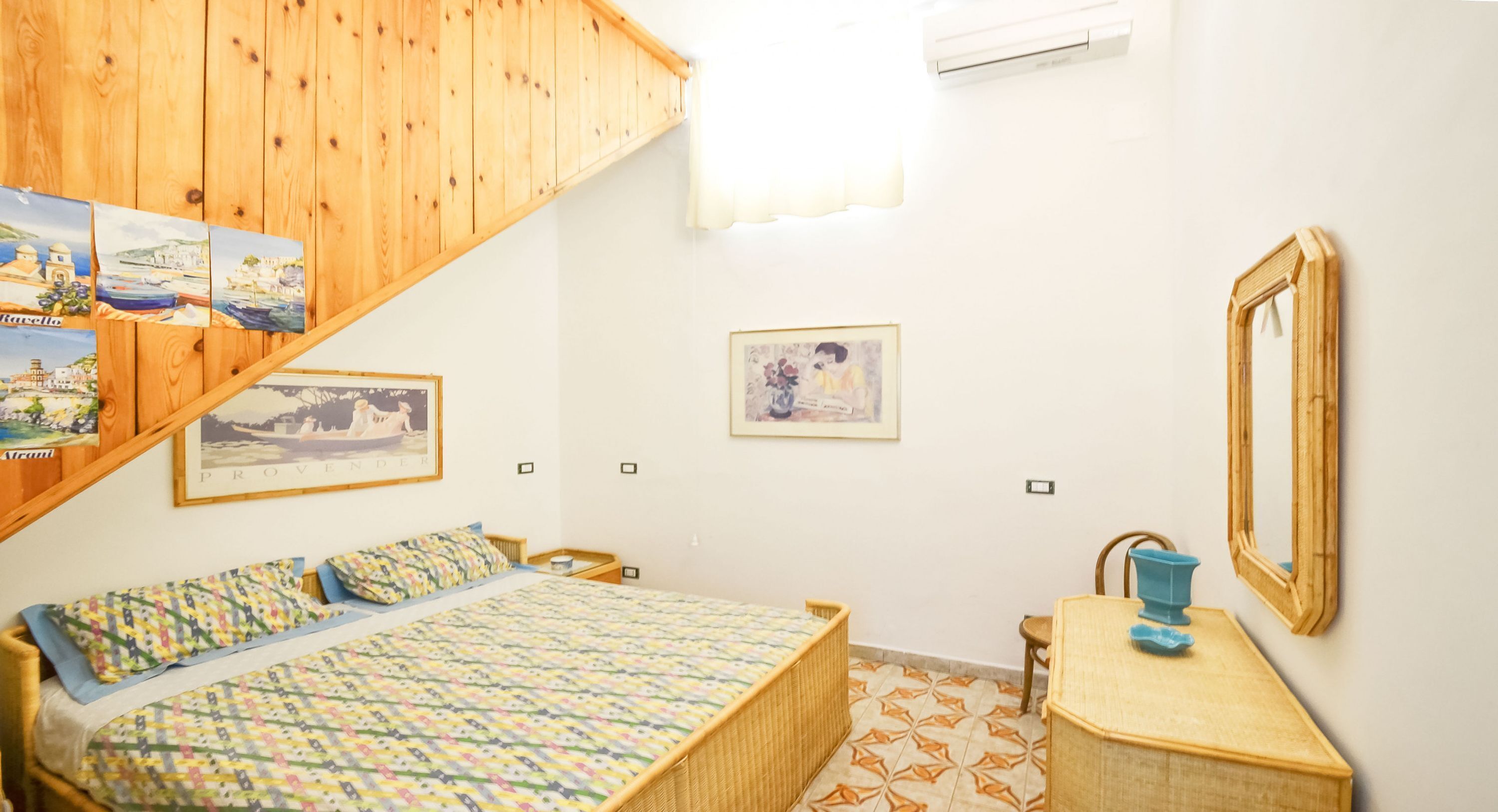 Ein Schlafzimmer mit einem Bett, einem kleinen Tisch, einem Stuhl, einem Spiegel und einer Wand mit gerahmten Bildern.