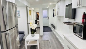 A modern kitchen with white cabinetry, a stainless steel refrigerator, a dining area with a white table and chairs, and a TV mounted on the wall. - Stylish 1 Bedroom Apartment close to Bloor West Village (Toronto)