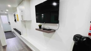 A modern living room with a mounted TV, a small shelf, and a black leather chair. - Stylish 1 Bedroom Apartment close to Bloor West Village (Toronto)