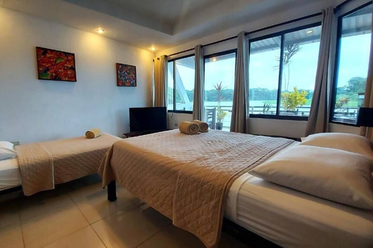 A hotel room with two beds, a flat-screen TV, and large windows offering a view of the outdoors.