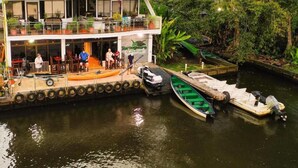 Un edificio de dos pisos con un restaurante en la planta baja y una terraza panorámica en el nivel superior. Varias embarcaciones están amarradas en el muelle.