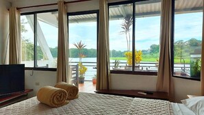 Habitación de hotel con cama, televisión y vista a un lago y vegetación.
