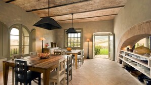 A spacious dining area with a rustic wooden table and chairs, a hanging light fixture, and a view through an arched doorway to the outdoors. - Villa Olimpia in Sarteano (Sarteano)
