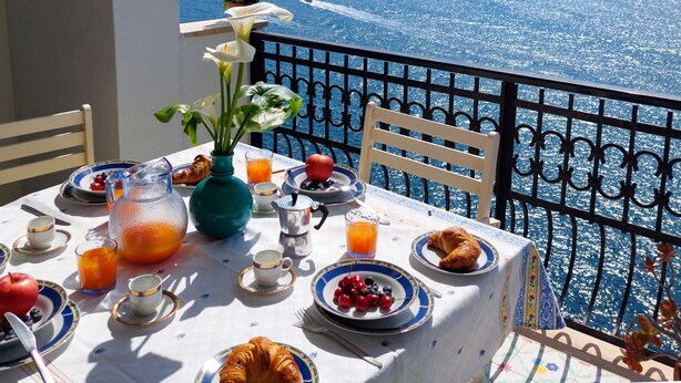 Ein Balkontisch mit Frühstücksleckereien, eine Vase mit Blumen und Blick auf das Meer.
