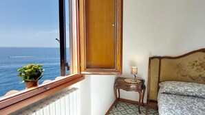 Ein Balkon mit Holztür, einem kleinen Tisch mit Lampe, einem Bett mit gemusterten Betttextilien und einem Blumentopf.