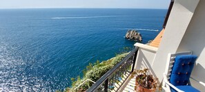 A balcony with a view of the sea, a rock formation, and a chair with cushions. - Casa Gianna in Praiano (Praiano)