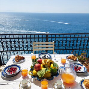 A table set with breakfast items including croissants, fruits, and juice, overlooking a scenic ocean view. - Casa Gianna in Praiano (Praiano)