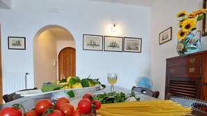 Ein Esstisch mit frischen Tomaten, Spinat und Pasta. An den Wänden hängen Bilder in Rahmen und auf einem Schrank steht eine Vase mit Sonnenblumen.