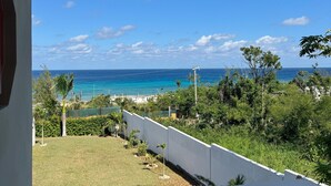 A balcony with a view of the ocean and a grassy area with trees. - Blue Turquoise Sea Villa (Montego Bay)