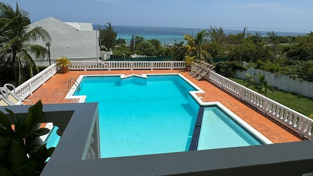 A swimming pool with a view of the ocean, surrounded by a white fence and palm trees. - Blue Turquoise Sea Villa (Montego Bay)