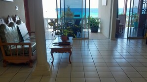 A spacious room with a tiled floor, a wooden bench, a table with a plant, and a view of the ocean through large glass doors. - Blue Turquoise Sea Villa (Montego Bay)