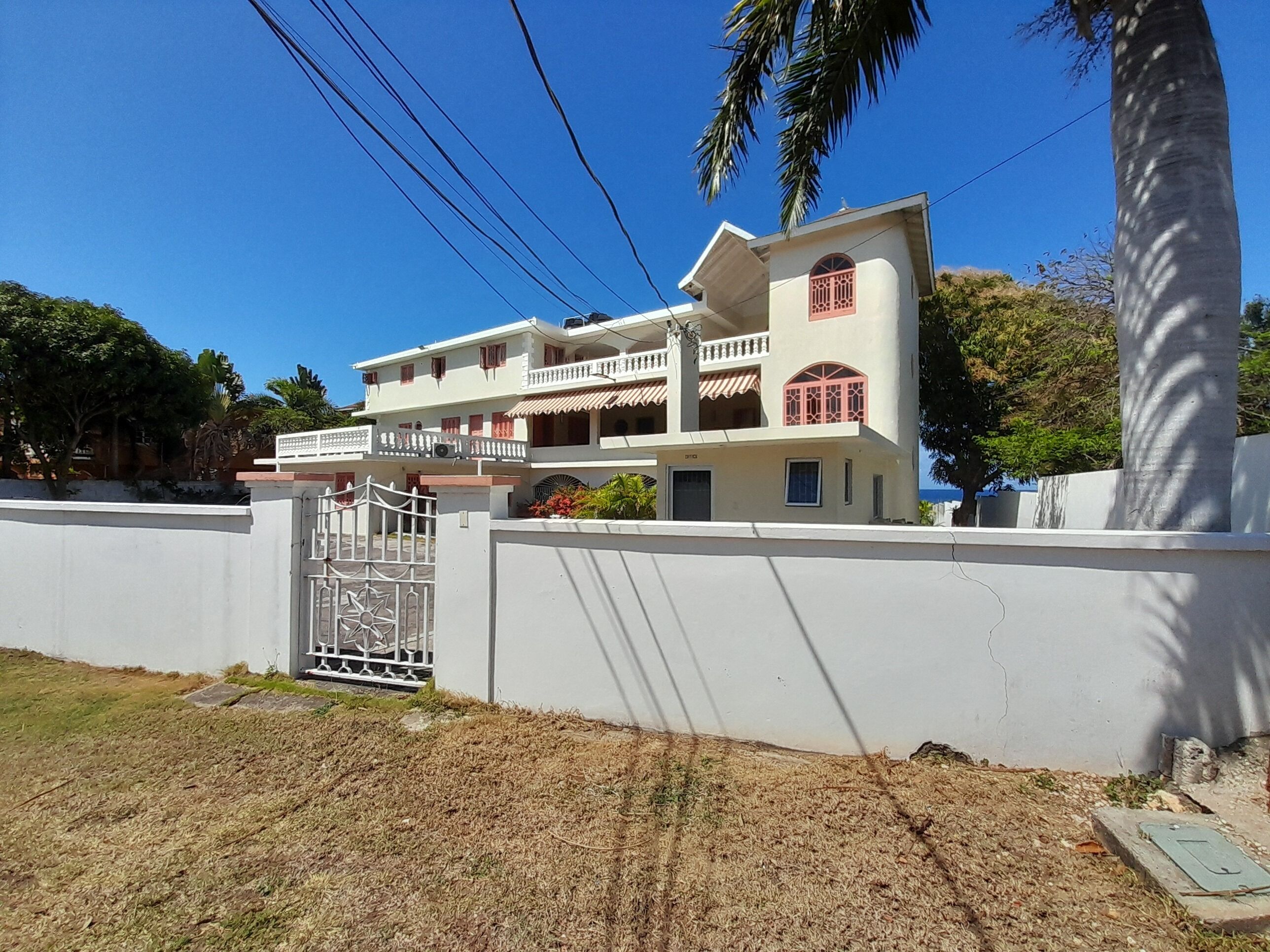 A two-story house with a white exterior, a gated entrance, and a balcony.