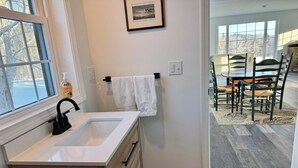 A bathroom with a white sink, wooden cabinetry, a towel rack with a white towel, and a framed picture on the wall. - Beautiful new studio with amazing views - peaceful but close to everything! (Weston)