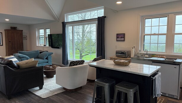 A modern kitchen with a large window, a built-in oven, and a dining area with stools. - Beautiful new studio with amazing views - peaceful but close to everything! (Weston)