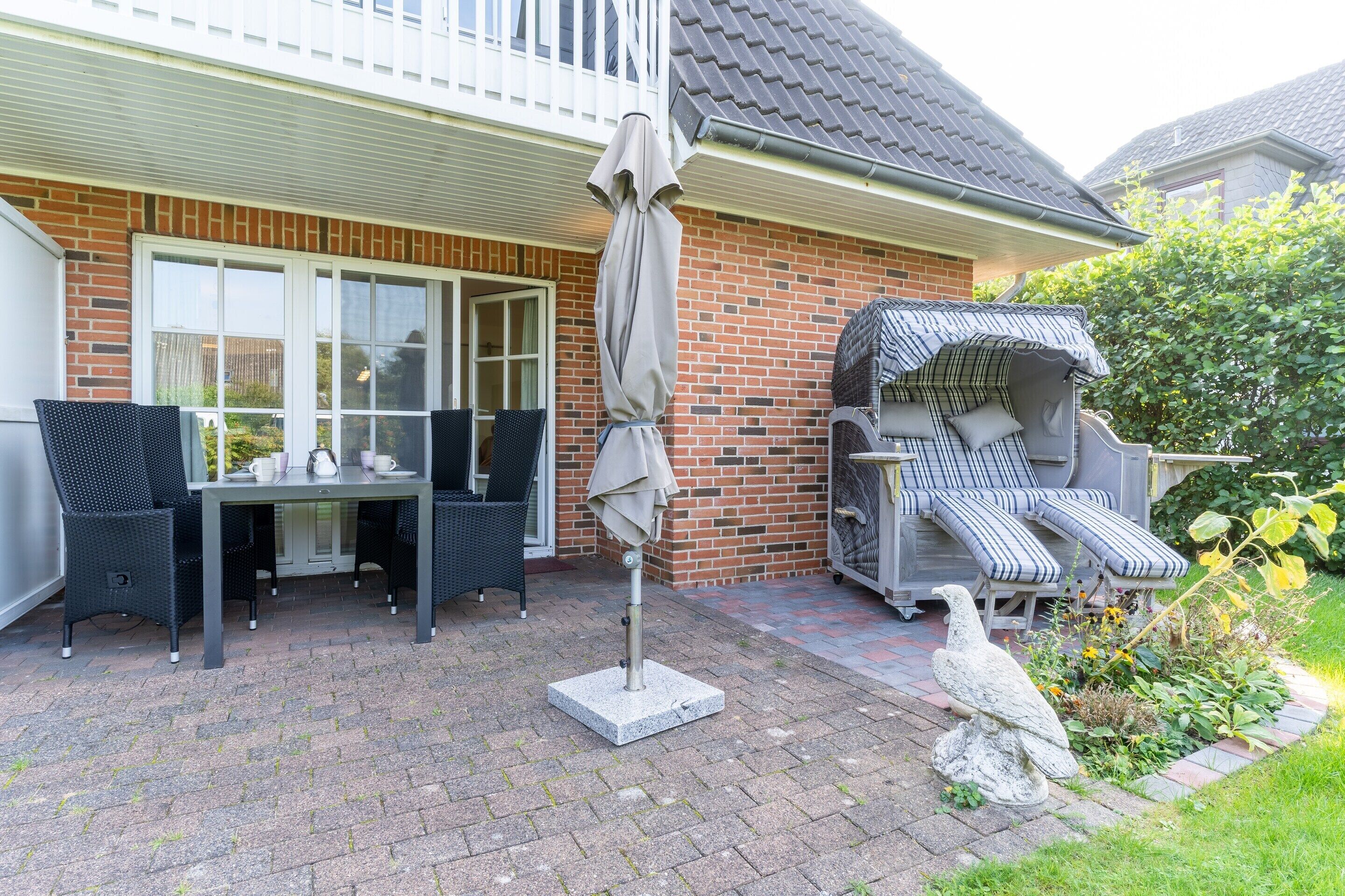 A patio with outdoor furniture, a covered seating area, and a garden with a bird statue.