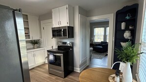 Eine moderne Küche mit weißen Schränken, einer schwarzen Mikrowelle und einem Backofen. Es gibt einen Essbereich mit einem Holztisch und Stühlen.