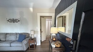Ein Wohnzimmer mit einer Couch, einem Couchtisch, einer Lampe und einer Tür mit Spiegel.