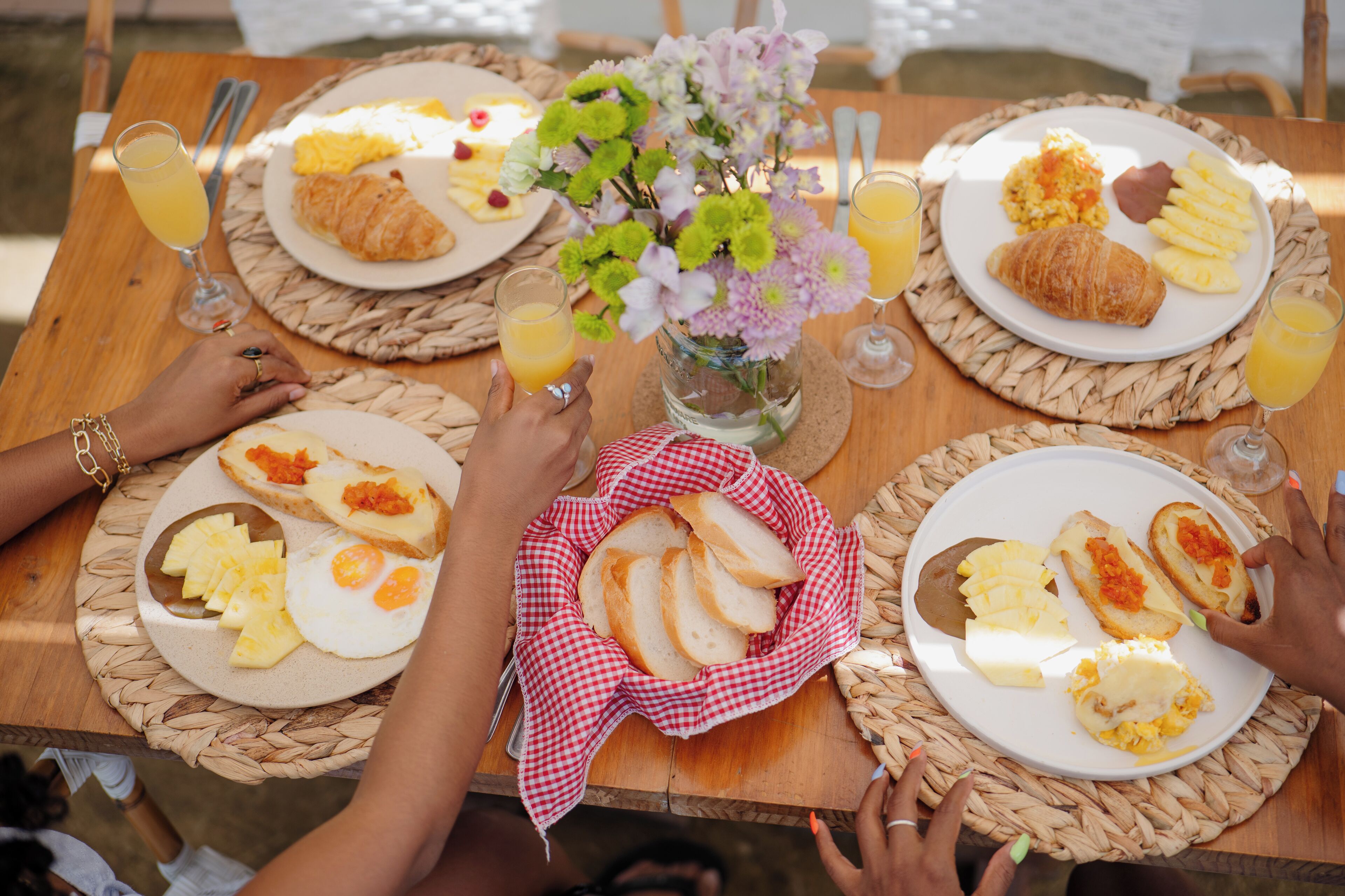 A table set with breakfast plates, including croissants, eggs, and fruit, with a vase of flowers in the center.