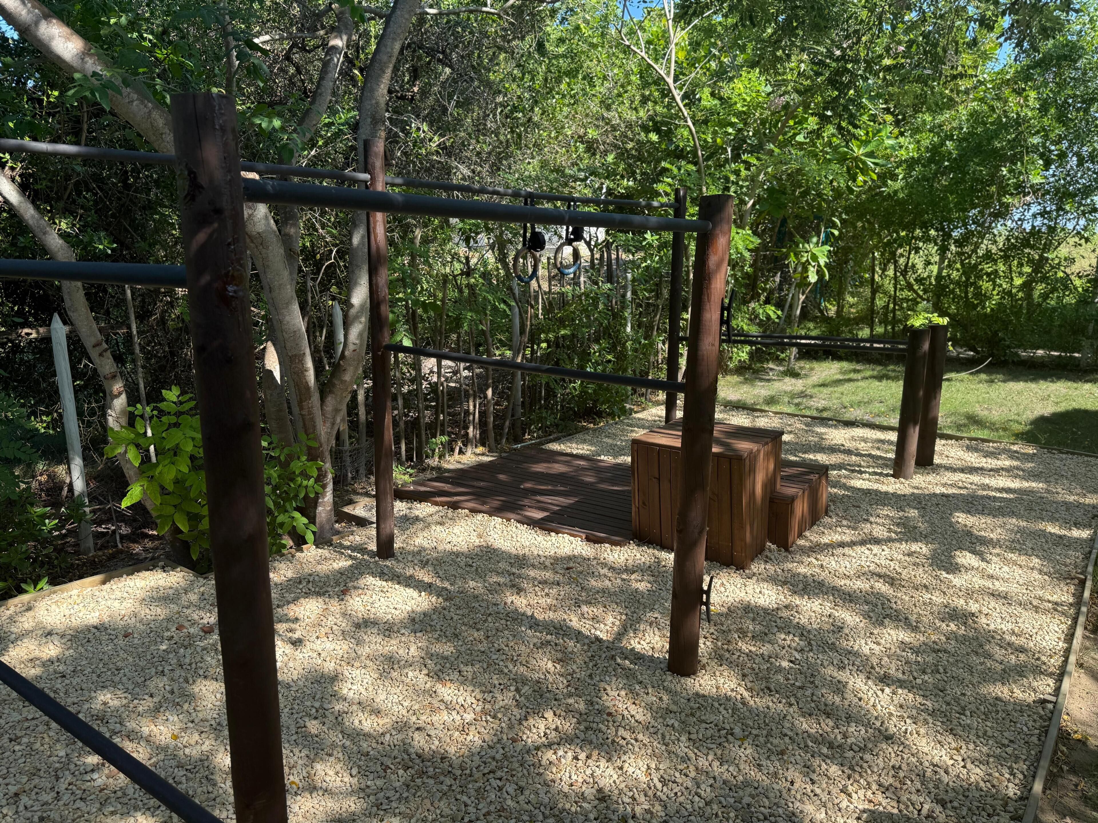 Un parque infantil con estructuras de madera, un puente colgante y suelo de grava.