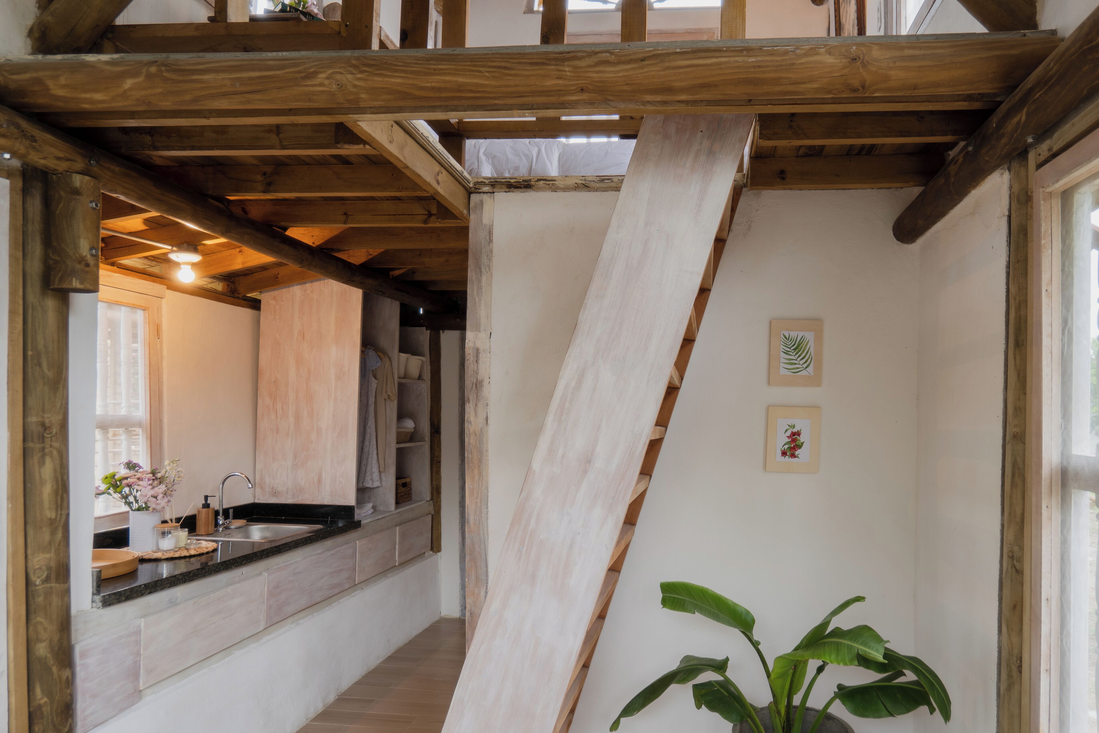 A narrow hallway with wooden beams, a kitchen area with a sink and countertop, and a potted plant.