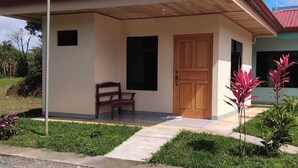A single-story house with a red roof, a front door, and a bench outside. - Cabinas El Pilon Rio Celeste (Katira)
