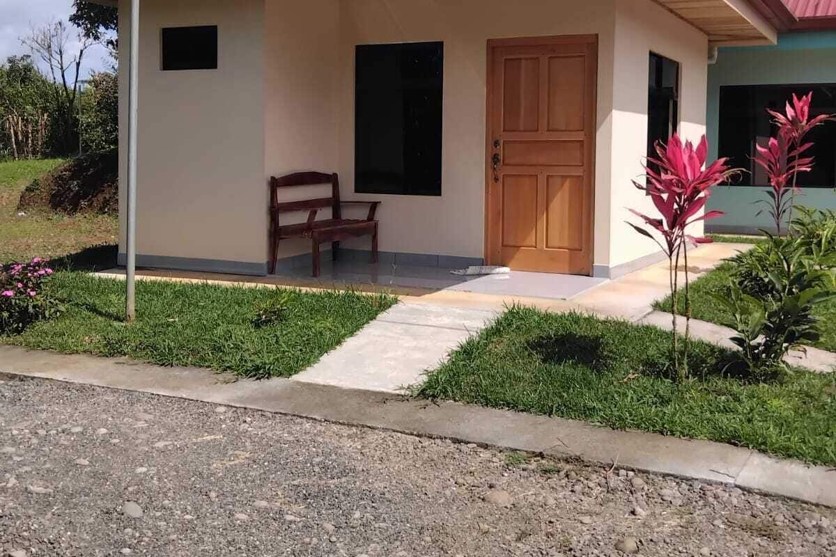 Una casa de un piso con techo rojo, puerta principal y un banco en el exterior.