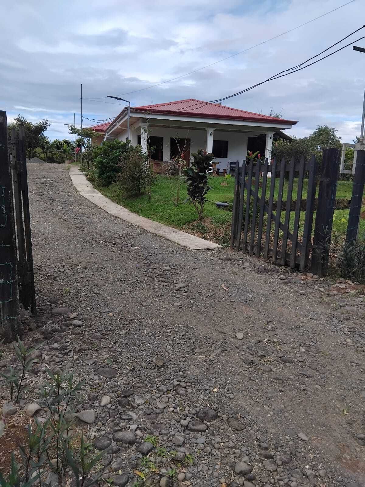 A gravel driveway leading to a house with a red roof and a wooden fence.